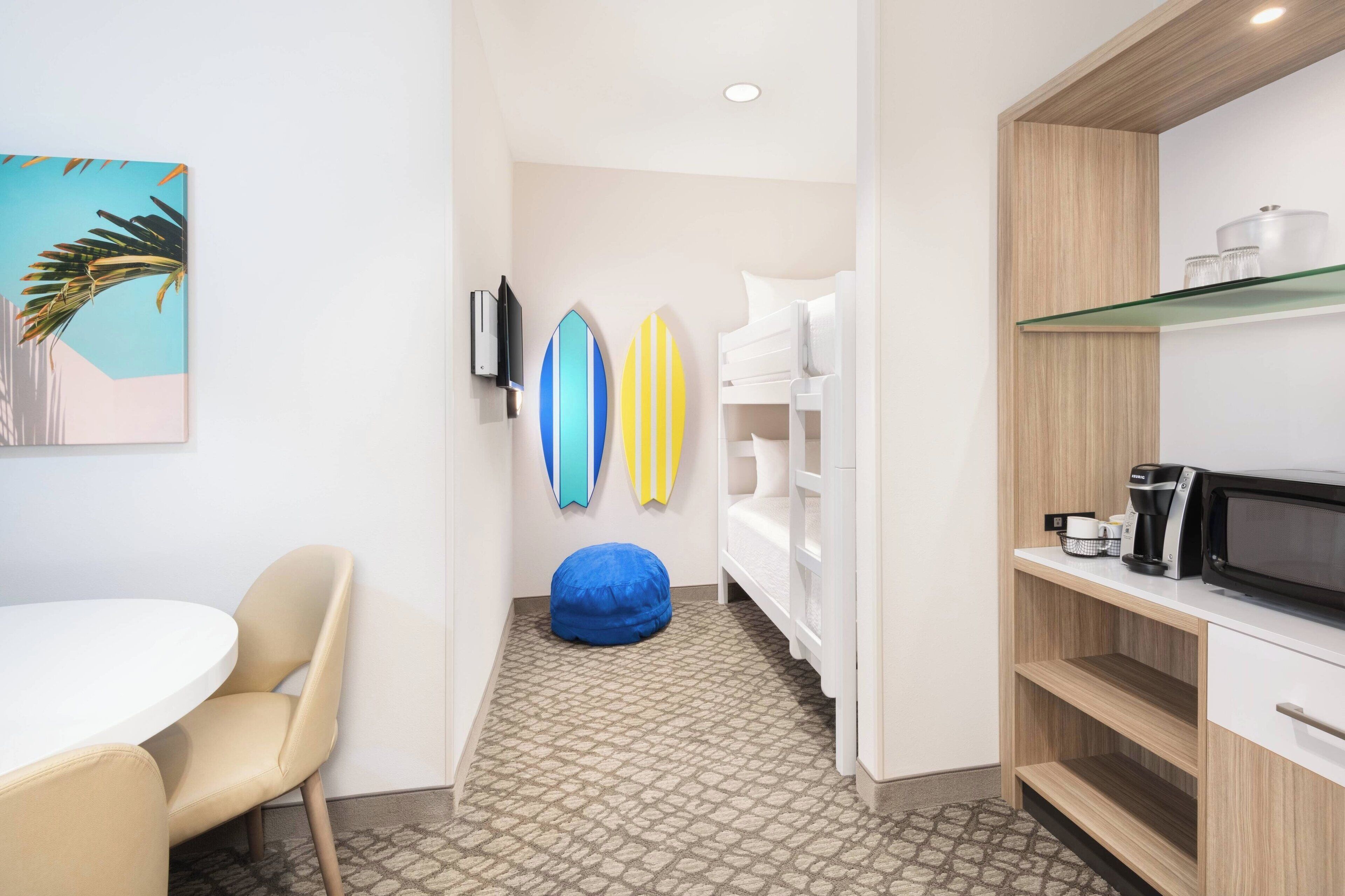 A room with a round table, a blue bean bag, a white bunk bed, and surfboards on the wall.