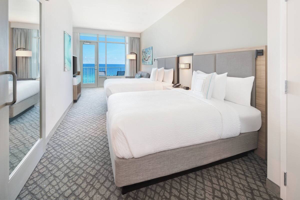 A hotel room with two beds, a balcony with a view, and a large window.