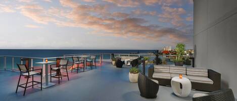 Una terraza en la azotea con asientos al aire libre, piscina y vistas al océano.