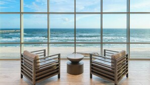 Una habitación con amplios ventanales que dan a una playa y al océano, con dos sillas de madera y una mesa redonda.