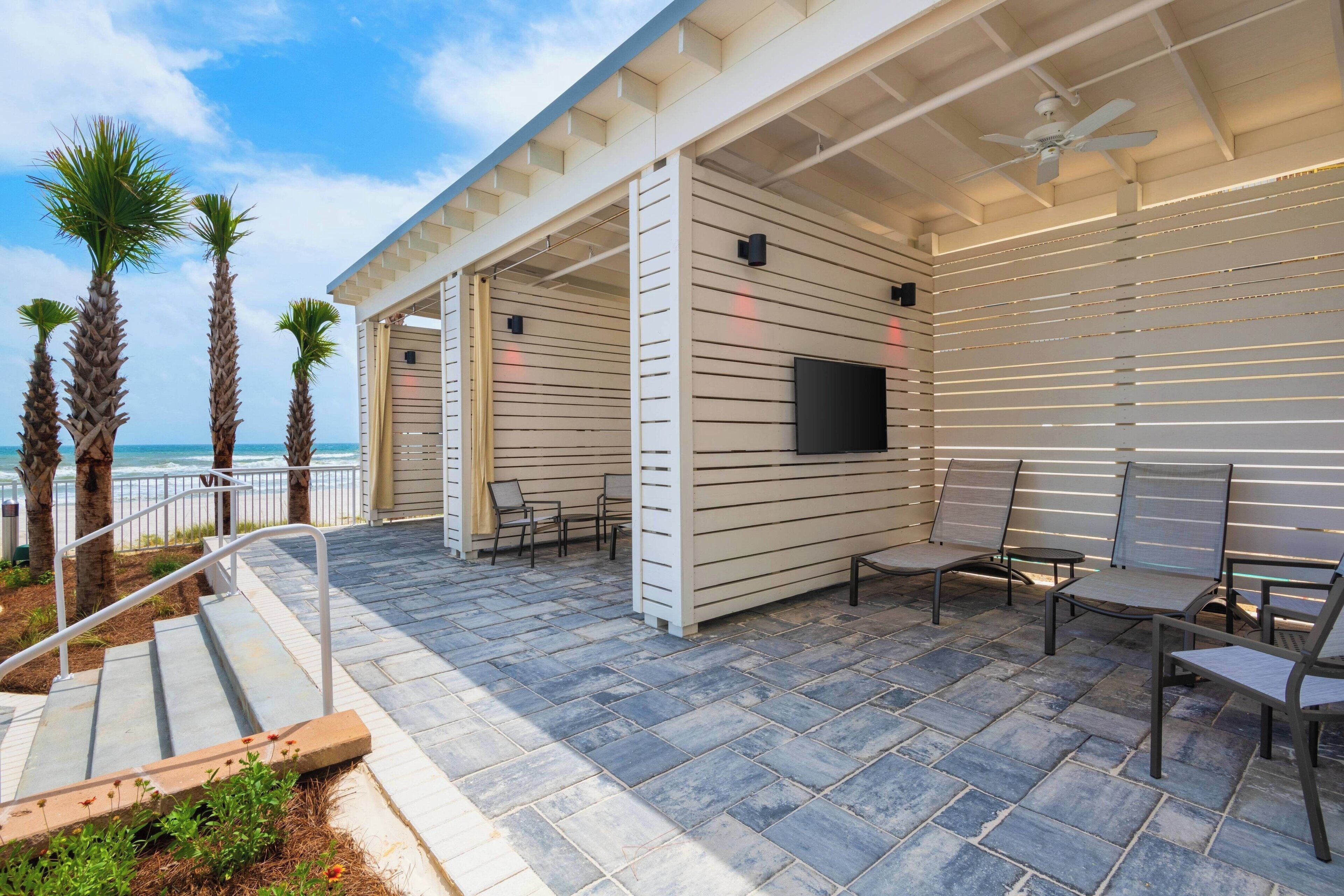 A covered outdoor seating area with a TV, chairs, and a view of the ocean.