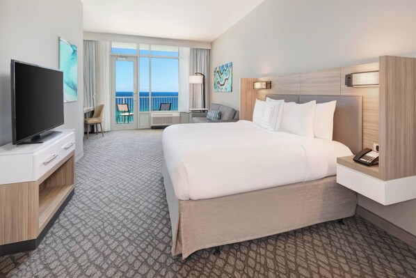 Une chambre d’hôtel avec un grand lit, une télévision, un bureau et un balcon donnant sur l’océan.