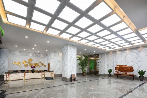 A spacious lobby with a marble reception desk, a large fish sculpture, and a high ceiling with skylights.