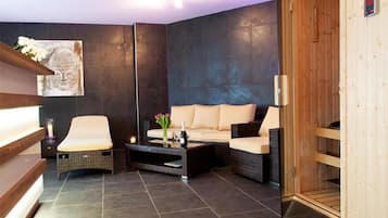 A modern spa room with a sofa, two chairs, a coffee table, and a wooden sauna.