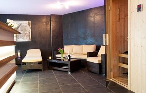 A modern spa room with a sofa, two chairs, a coffee table, and a wooden sauna.