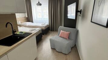 Ein kompakter Wohnraum mit Küchenzeile, einem Bett, einer Sitzecke und einem fenster mit Vorhängen.