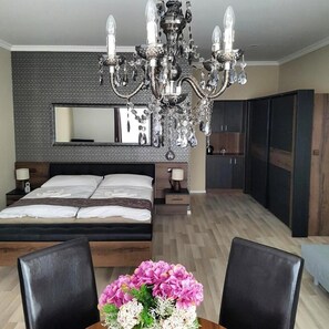 A modern bedroom with a large bed, a chandelier, a dresser, and a mirror.