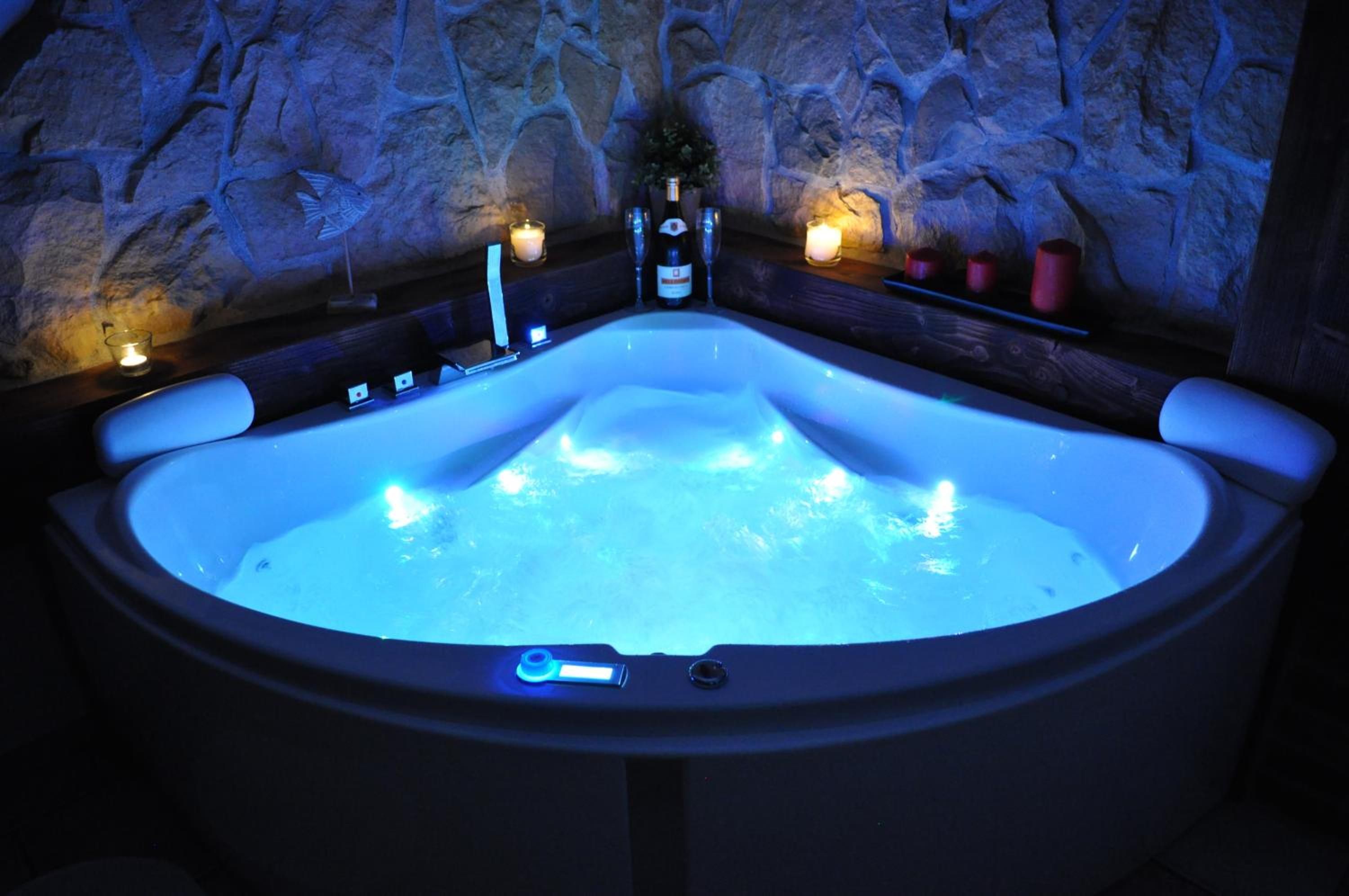 Un jacuzzi con un fondo de pared de piedra, una vela y una botella de vino.