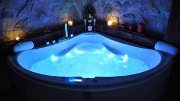 Un jacuzzi con un fondo de pared de piedra, una vela y una botella de vino.