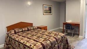 A bedroom with a wooden bed, a desk with a chair, and a painting on the wall. - Palms Motel (Emeryville)