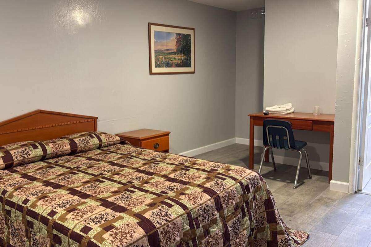 A bedroom with a wooden bed, a desk with a chair, and a painting on the wall.