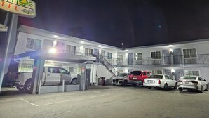 A hotel with a two-story structure, a covered parking area, and several cars parked in front. - Palms Motel (Emeryville)