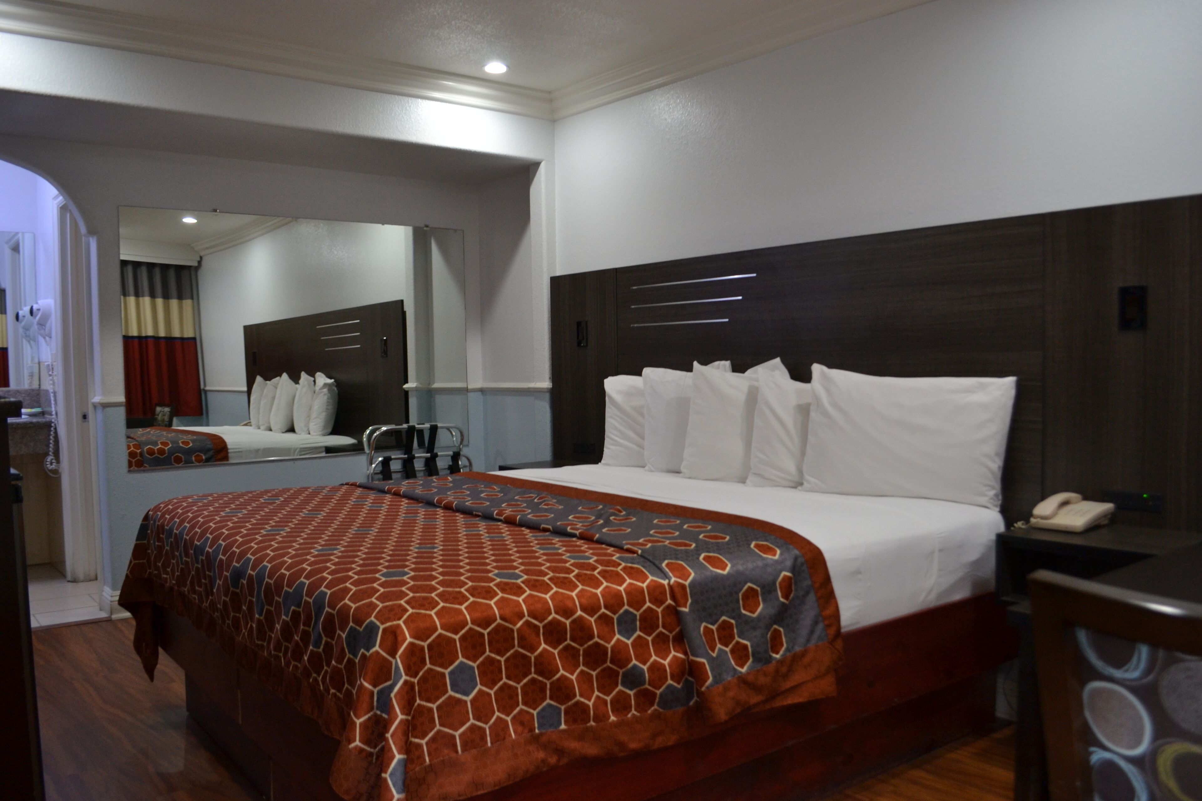 A hotel room with a large bed, a bedside table with a phone, and a mirror above the bed.