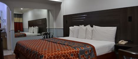 A hotel room with a large bed, a bedside table with a phone, and a mirror above the bed.