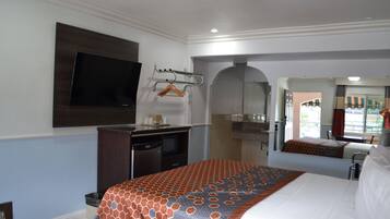 A hotel room with a bed, a desk with a flat-screen TV, a microwave, and a small kitchenette.