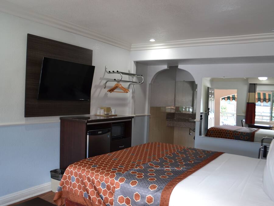 A hotel room with a bed, a desk with a flat-screen TV, a microwave, and a small kitchenette.