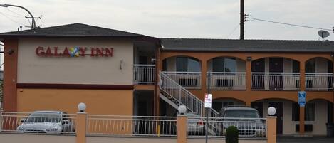 Un motel de dos pisos con un letrero que dice "GALAXY INN" y un estacionamiento con coches.