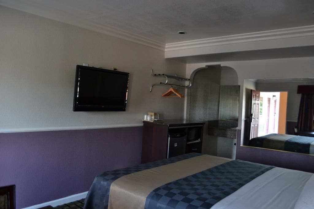 A hotel room with a bed, a desk, a television, a mirror, and a coat rack.