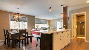 Cocina moderna con suelo de madera, una isla central e iluminación colgante.