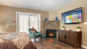 Una sala de estar moderna con chimenea, televisor montado en la pared y un amplio ventanal con persianas.