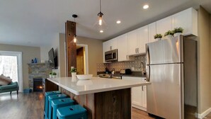 Una cocina moderna con una isla central, electrodomésticos de acero inoxidable y taburetes de bar azules.