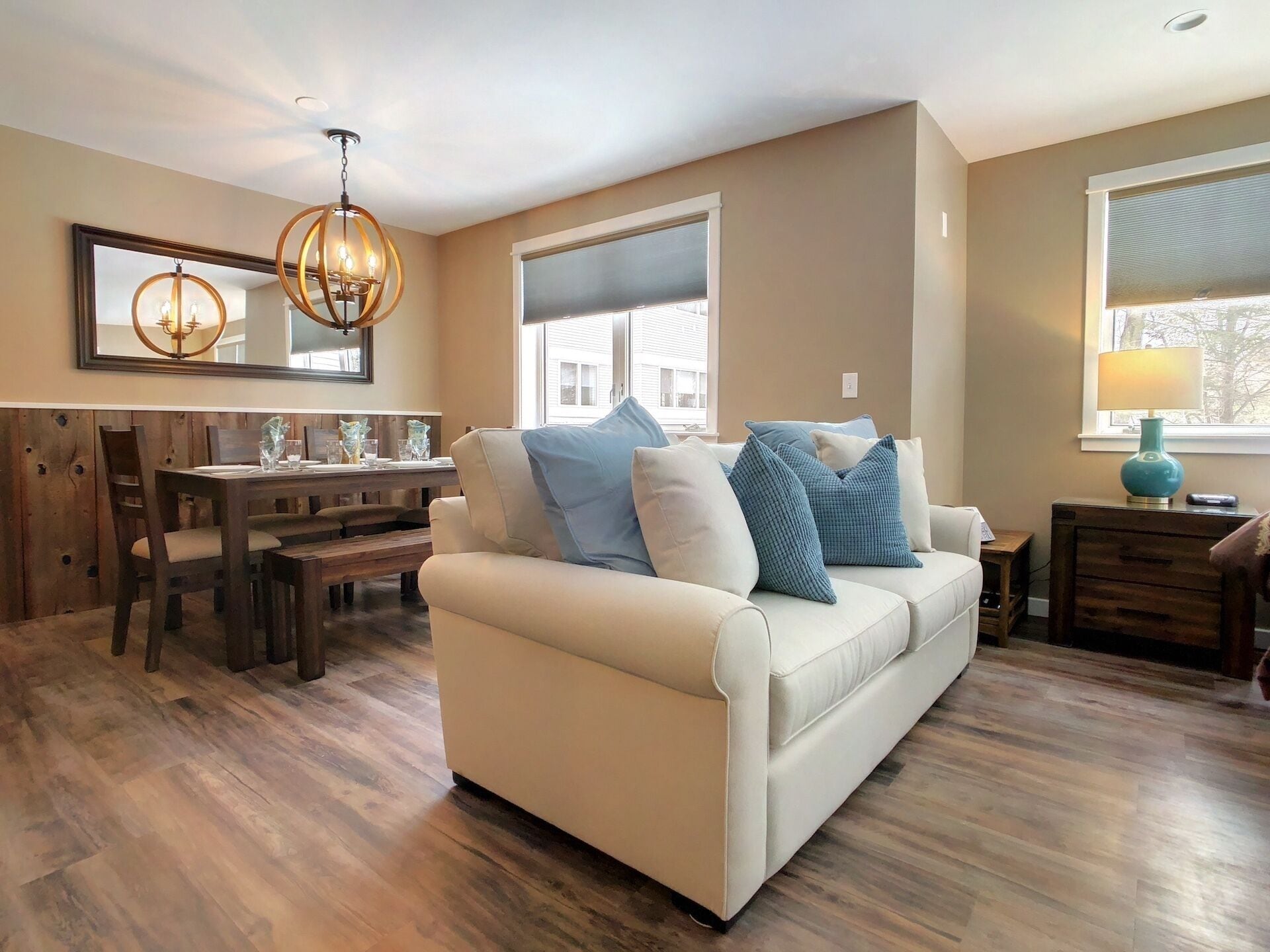 A living room with a beige sofa, a wooden dining table, and a chandelier.