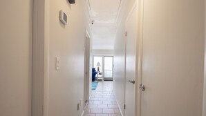 A narrow hallway with white walls and a tiled floor leading to a room with a large window and a blue rug. - Enjoy Family Memories - Great Outdoor Decks And Backyard; A Few Houses To Beach (Surf City)