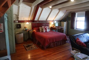 Une chambre mansardée chaleureuse avec un plancher en bois, une couvre-lit rouge et un canapé en cuir.