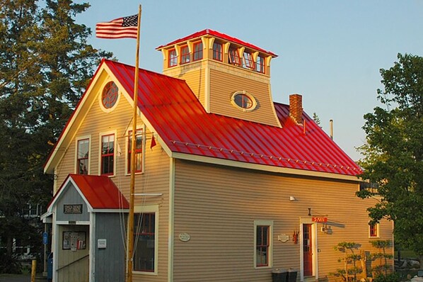 Un bâtiment à deux étages, doté d’un toit rouge et d’un revêtement beige, et surmonté d’une petite structure en forme de tour au deuxième étage.