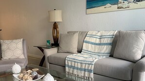 A living room with a glass coffee table, a grey sofa, and a painting of a beach scene. - Beautiful/Spacious Ocean Reserve Sunny Isles Beach #STR-02481 (Sunny Isles Beach)