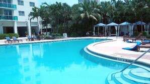 A clear blue pool with lounge chairs and umbrellas, surrounded by palm trees and a building with multiple balconies. - Beautiful/Spacious Ocean Reserve Sunny Isles Beach #STR-02481 (Sunny Isles Beach)