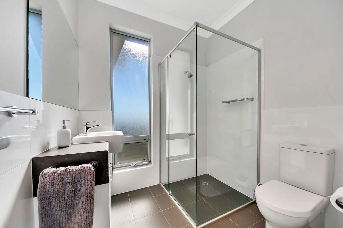 A modern bathroom with a glass shower enclosure, a toilet, a sink with a mirror, and a window.