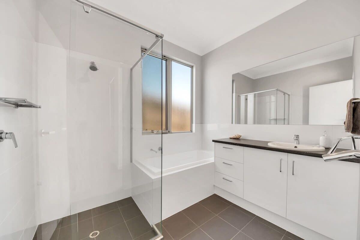 A modern bathroom with a glass shower enclosure, a large mirror, and a white sink.