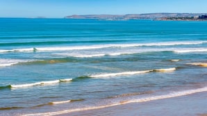 Une plage avec des vagues, un ciel dégagé et une terre lointaine à l’horizon.