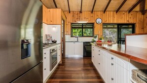 Cocina con armarios de madera, refrigerador de acero inoxidable, un reloj en la pared y ventana con vista a follaje.