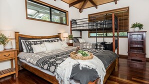 Un dormitorio con una cama grande, cabecera de madera, una ventana, una mesita de noche y un armario de madera.