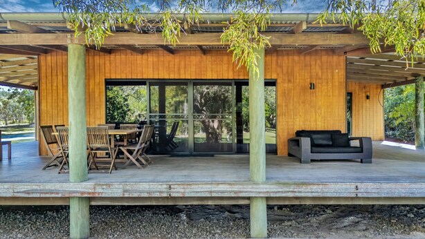 Un espacio al aire libre techado con piso de madera, una mesa con sillas y un sofá.