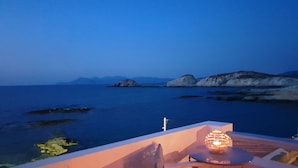 A terrace with a table and chair overlooking a calm sea and rocky outcrops.