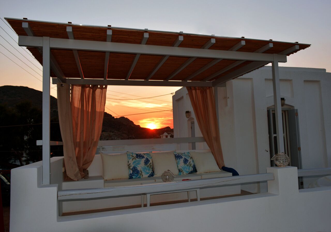 A white building with a wooden pergola and a white bench with cushions.