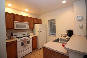 A compact kitchen with wooden cabinets, a microwave, a refrigerator, a stove, and a sink. - Venetian Bay Townhouse with Room for Ten - VB006 (Kissimmee)