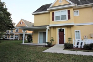 A two-story residential building with a front porch, a red door, and a white picket fence. - Venetian Bay Townhouse with Room for Ten - VB006 (Kissimmee)