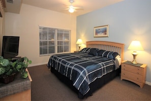 A bedroom with a bed, two bedside tables with lamps, a ceiling fan, a window with blinds, a television, and a plant. - Venetian Bay Townhouse with Room for Ten - VB006 (Kissimmee)