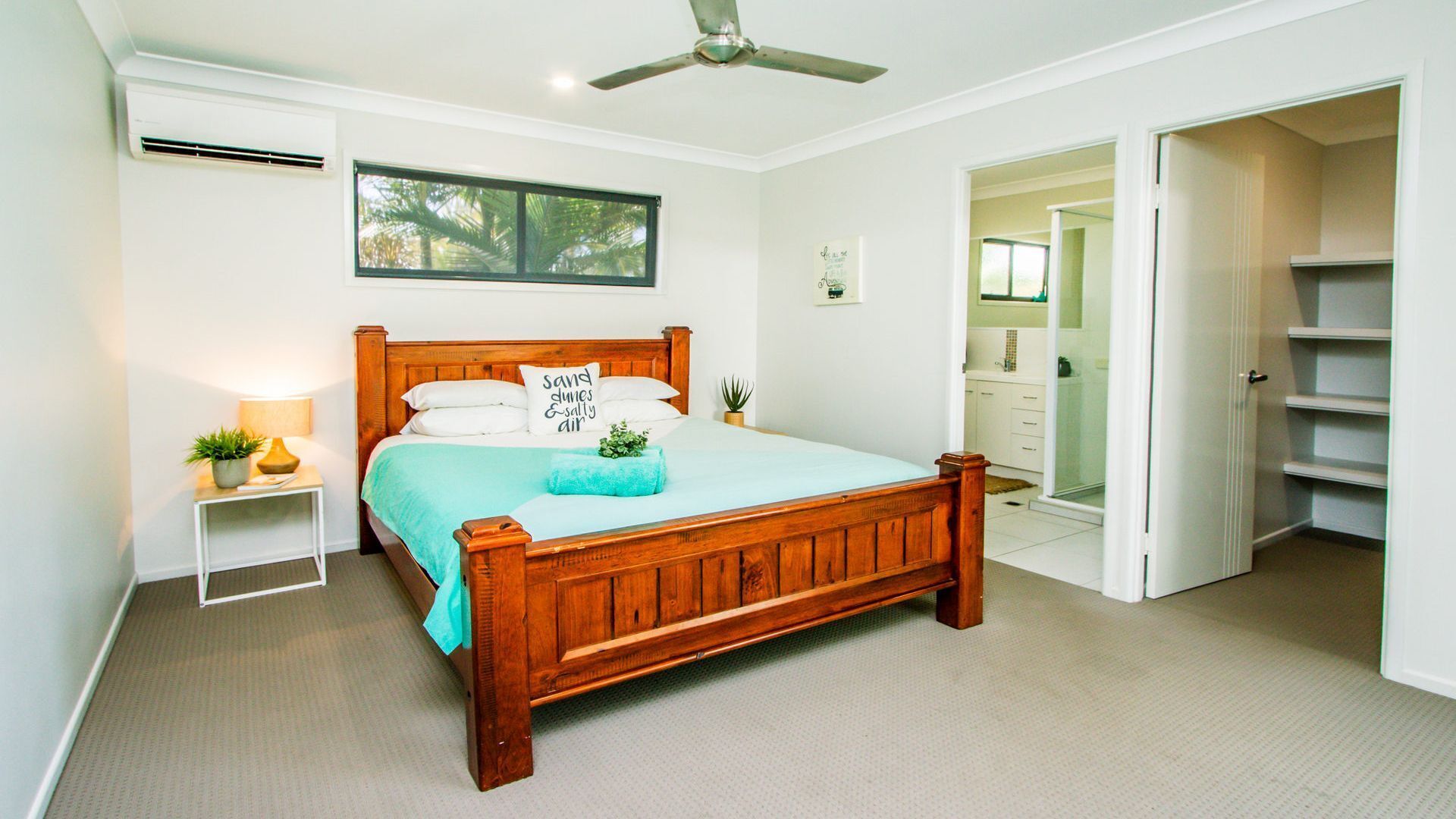 A bedroom with a wooden bed, a ceiling fan, a window, and a bathroom visible through an open door.