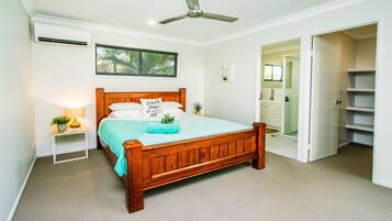 A bedroom with a wooden bed, a ceiling fan, a window, and a bathroom visible through an open door.