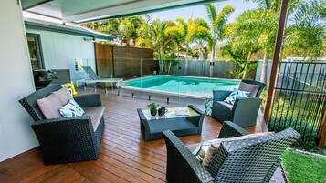 An outdoor patio with wicker furniture, a pool, and a view of palm trees.