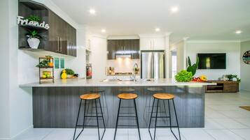 A modern kitchen with a central island, bar stools, a refrigerator, and a TV mounted on the wall.