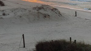 Ein Strand mit Sonnenuntergang, Sanddünen und einem Holzpfosten.