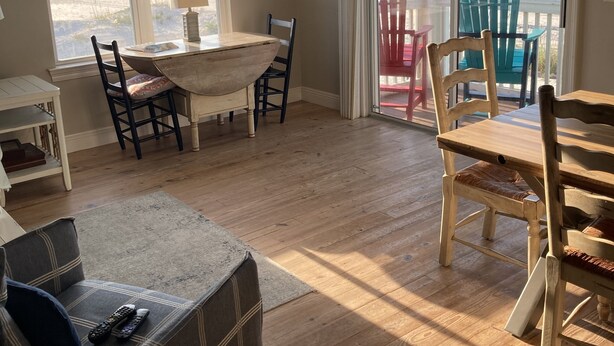 Ein Zimmer mit Holzboden, einem Esstisch mit Stühlen, einer Couch und Blick auf den Ozean durch eine Schiebetür.