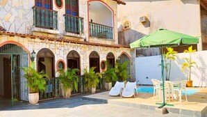 Un edificio de piedra con puertas arqueadas, un área de piscina con sillones de descanso y plantas en macetas.