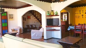 Una sala de estar acogedora con un sofá, sillas, un televisor y una escalera que lleva a otra habitación.